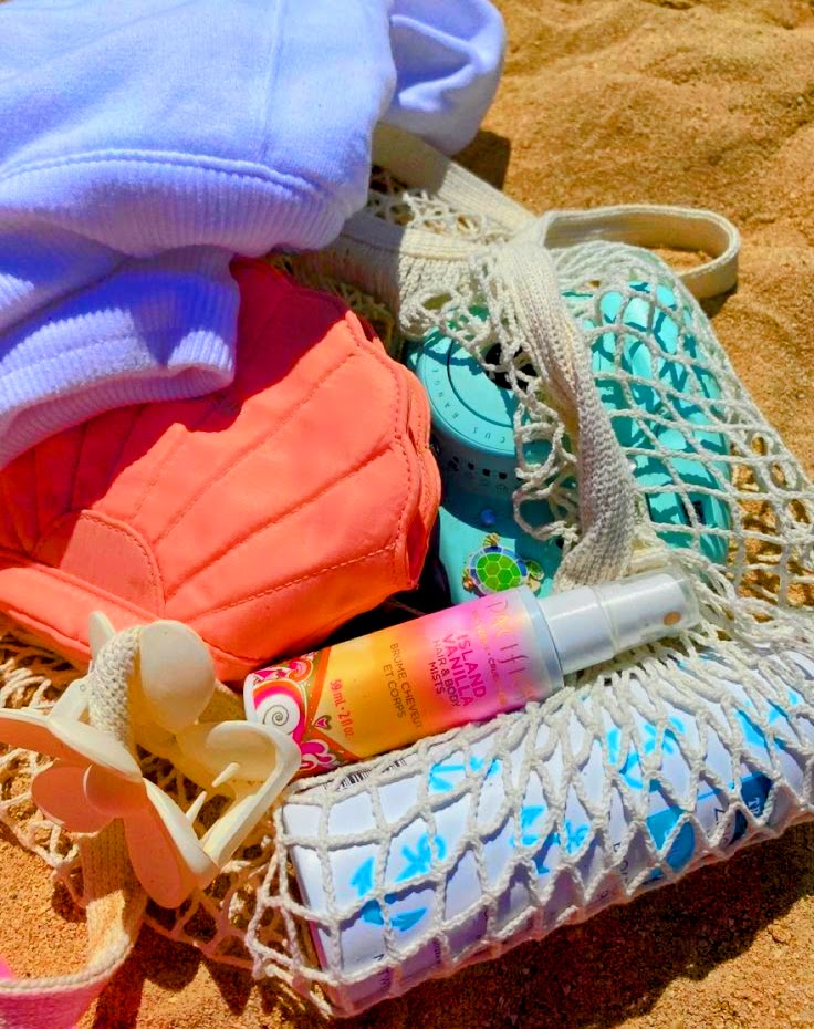 Woven beach bag with coral bikini top, sunscreen bottle, and accessories on sandy beach