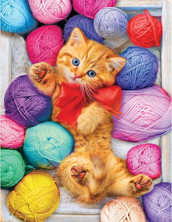 Orange kitten with blue eyes surrounded by colorful yarn balls