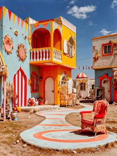 Colorful painted buildings with decorative art, bunting flags, and a red armchair on a painted courtyard