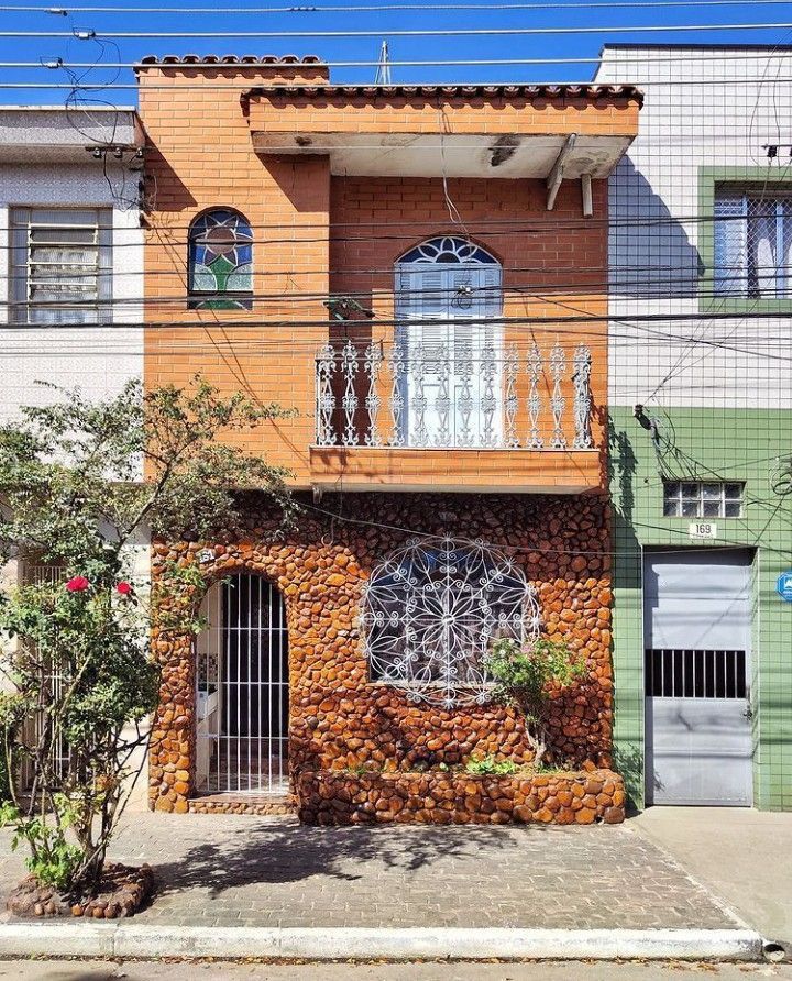 Narrow orange house with stone textured facade and decorative windows flanked by neighboring buildings