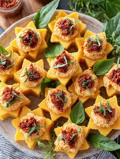 Star-shaped polenta appetizers topped with sun-dried tomatoes and basil on white platter