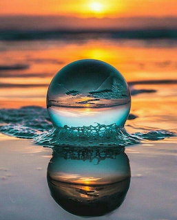 Crystal ball on wet beach sand reflecting an ocean sunset with golden and teal colors