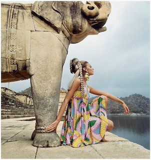 Woman in a colorful dress sitting beside a large stone elephant sculpture outdoors