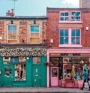 Colorful brick boutiques with teal and pink storefronts, flower boxes above, pedestrians on sidewalk