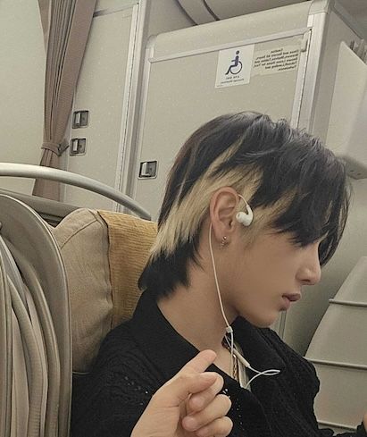Young man with dark hair listening to earbuds on airplane