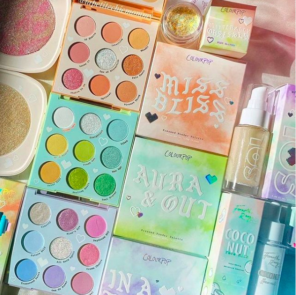 Colorful makeup palettes and beauty products arranged on a pink satin background
