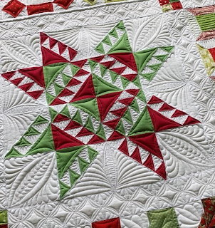Red and green geometric star quilt pattern with white quilted feather background