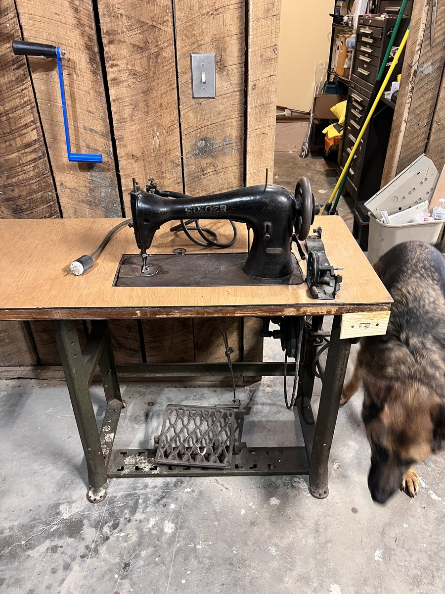 Vintage black industrial sewing machine on metal stand in a workshop with a dog beside it