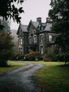 Gothic stone mansion with pointed rofs at the end of a wet driveway surrounded by green gardens on a fogy day