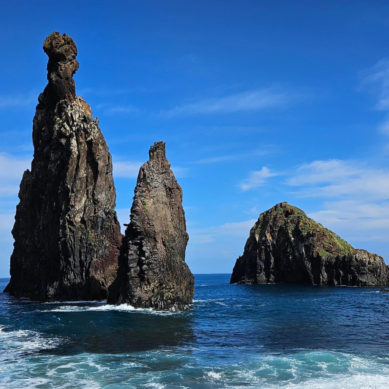 Tall volcanic rock formations emerging from blue ocean waters near Madeira coast
