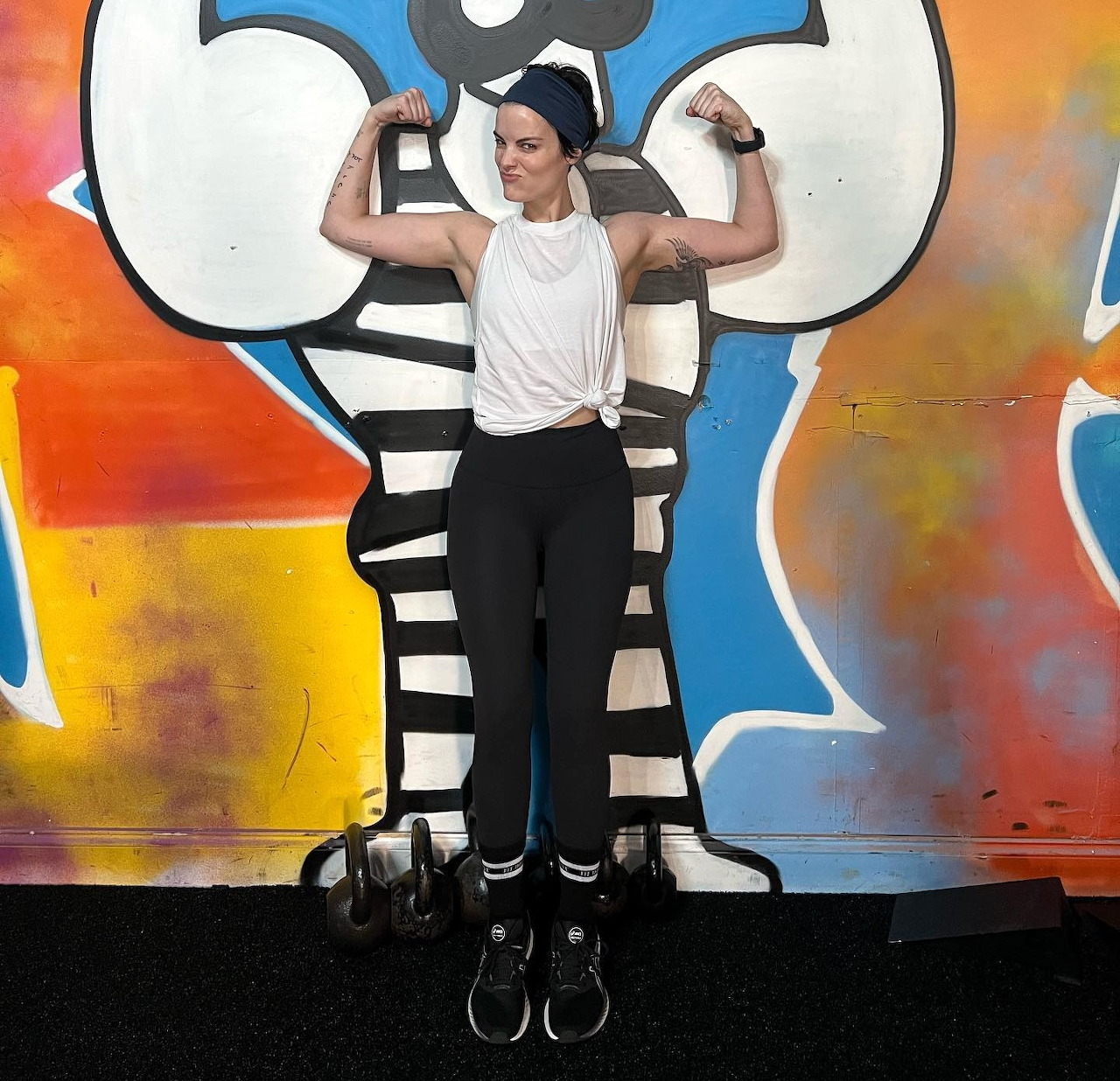 Woman flexing biceps in athletic pose against vibrant graffiti backdrop
