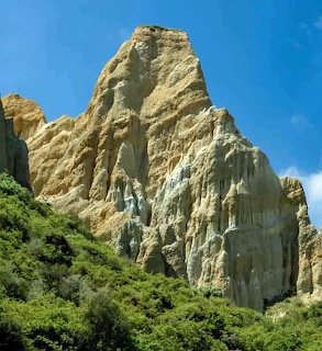 Rocky mountain cliff above green shrubs and blue sky
