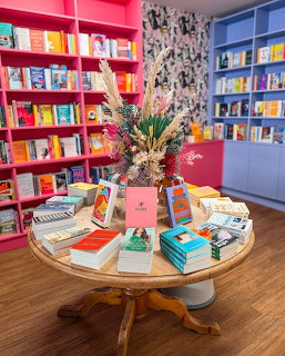 Modern bookstore interior with vibrant pink and blue shelves displaying books around a central wooden table