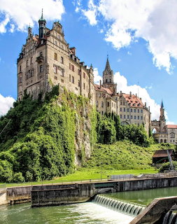 Sigmaringen Castle rising above a rocky cliff with a river weir and green hillside in Germany