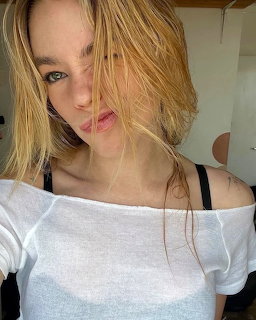 Portrait of young woman with blonde hair in white off-shoulder top looking at camera
