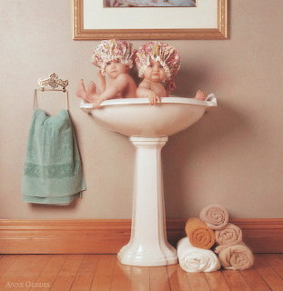 Two babies in a pedestal sink wearing flower bonnets in a bathroom