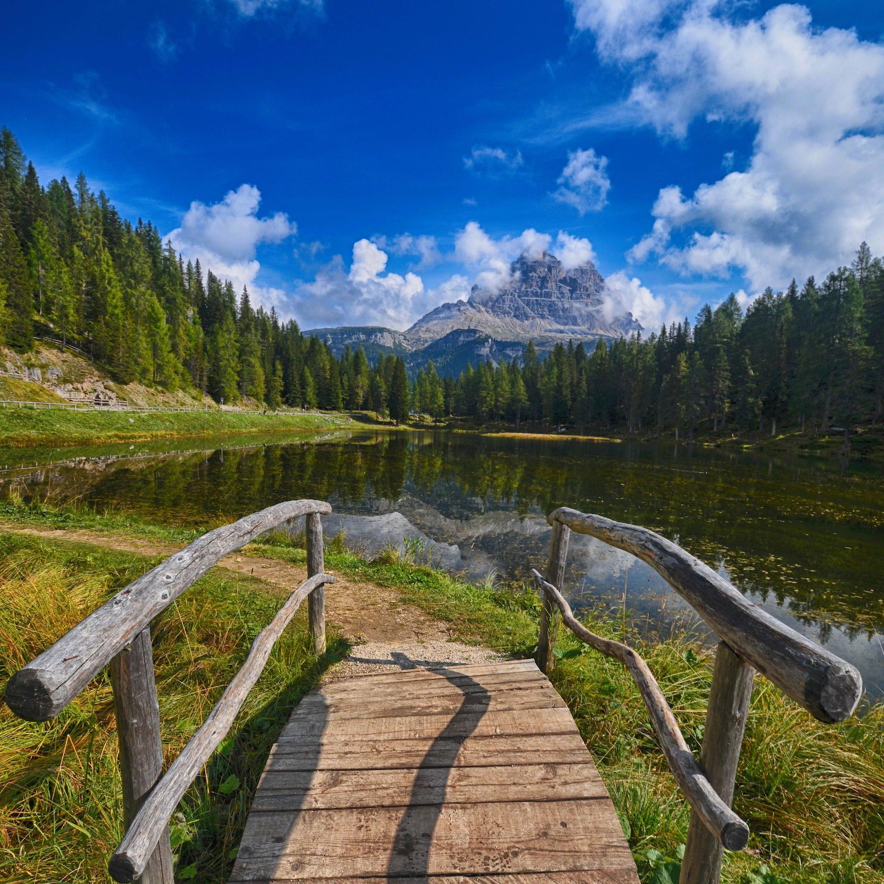 Wooden footbridge leading to a serene mountain lake surrounded by pine forests and rocky peaks