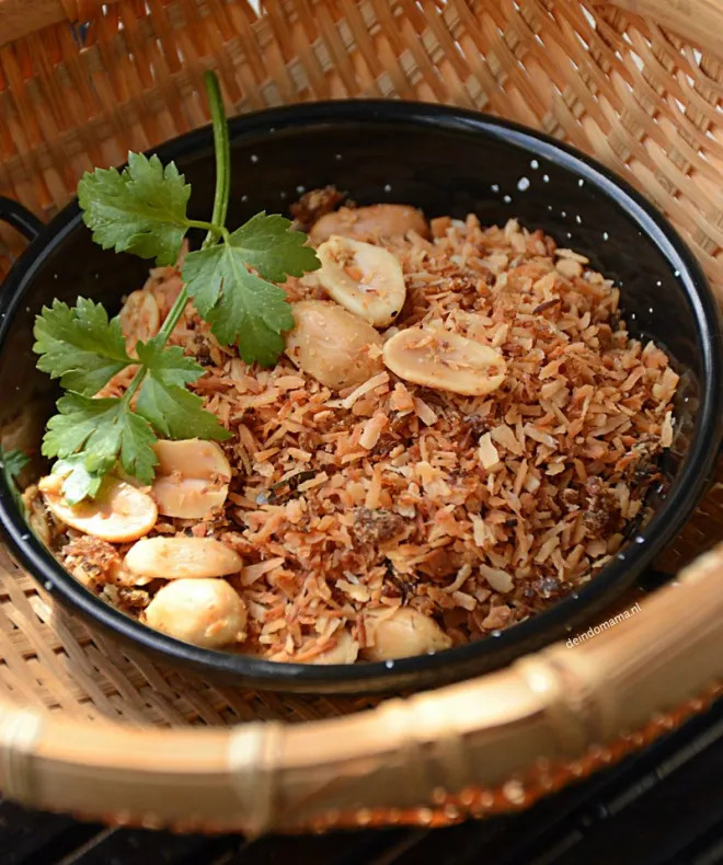 Bowl of seroendeng coconut condiment with peanuts and cilantro garnish on bamboo mat