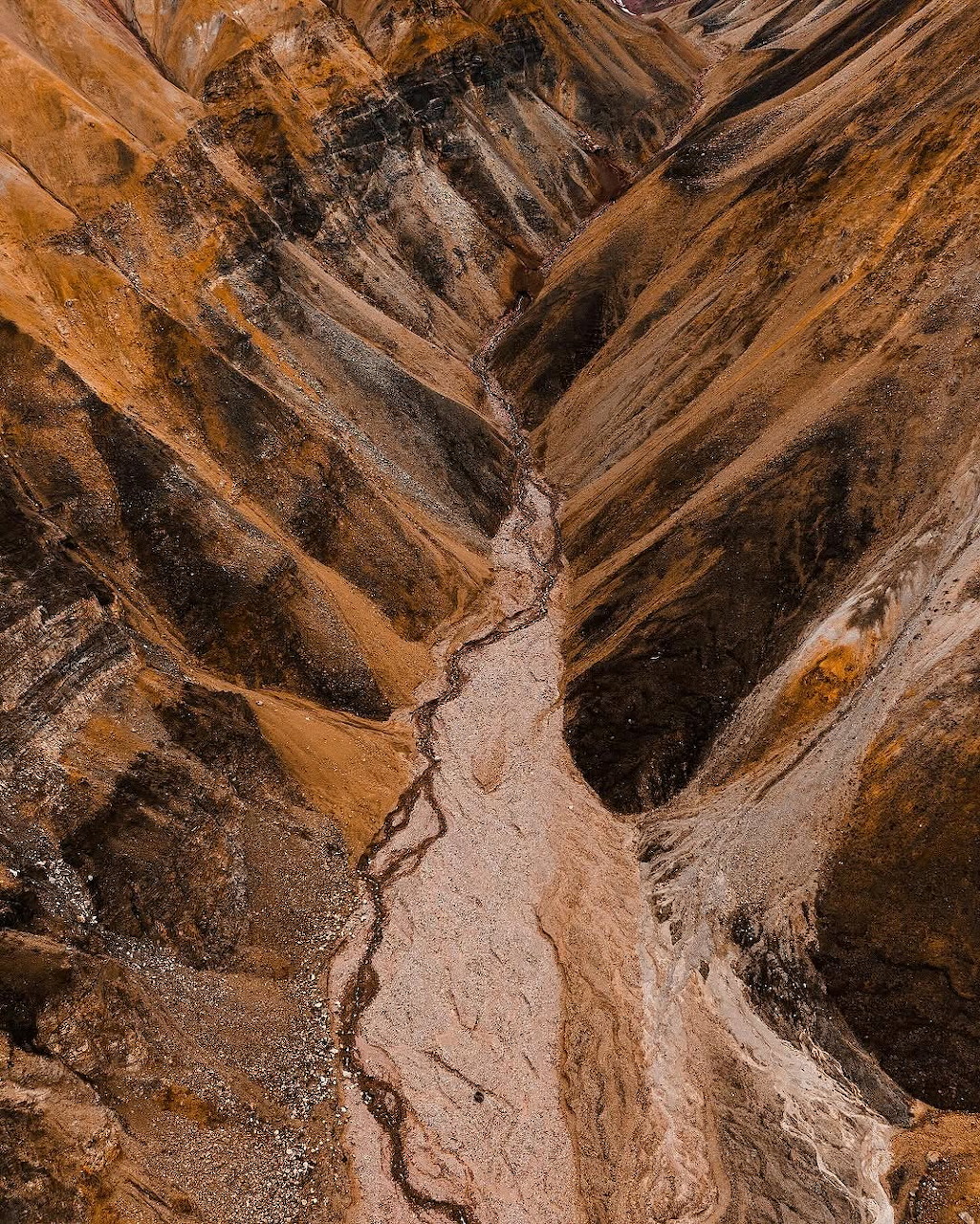 Aerial view of desert canyon with layered orange and brown rock formations and winding erosion path