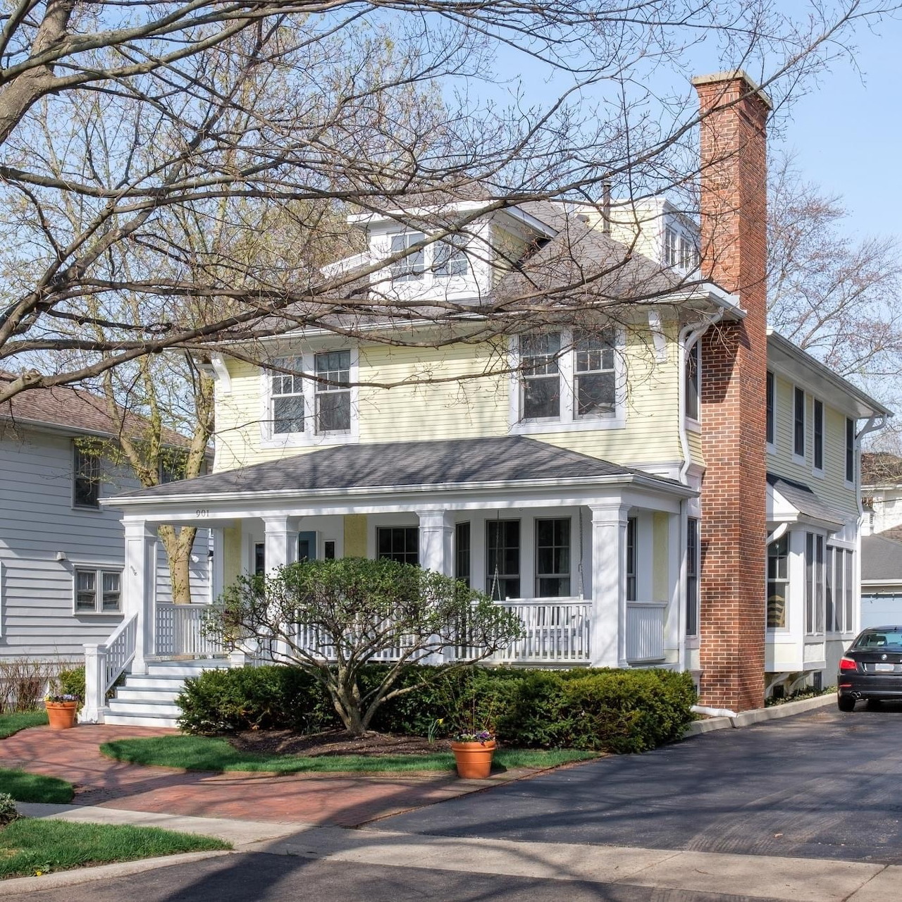 Yellow colonial style house with white porch and brick chimney in spring