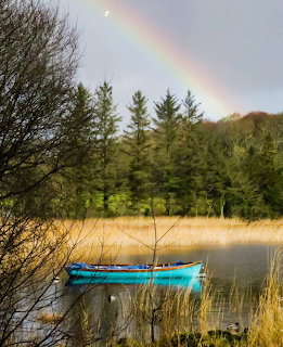 Blue boat on tranquil lake with rainbow and forest backdrop