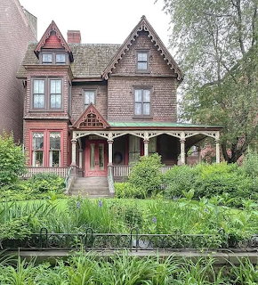Red brick Victorian house with ornate trim, porch, and a lush front garden