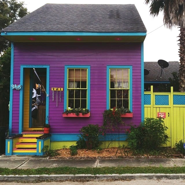 Small purple house with turquoise and yellow accents, window boxes, and colorful fence