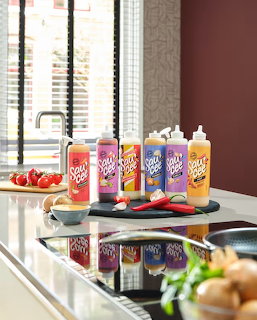 Colorful sauce bottles on wooden board with tomatoes and herbs on modern kitchen counter