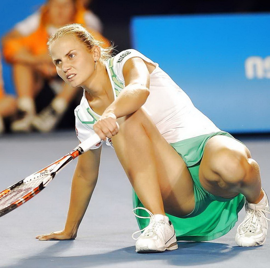 Female tennis player crouching on a court with a racket, wearing a white and green outfit