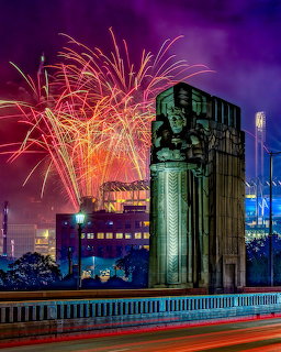 Fireworks over a city at night beside a tall mural-covered tower