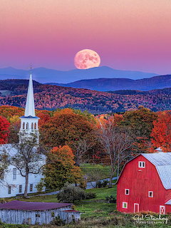 Full moon rising over mountains with white church steeple, red barn, and colorful autumn trees in Vermont