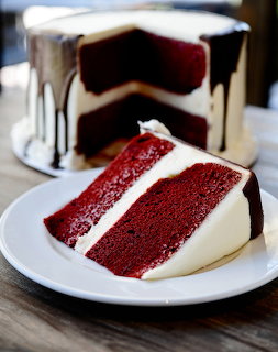 Slice of red velvet cake with white frosting and chocolate drizzle on white plate