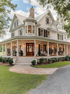 White Victorian house with wraparound porch, stone columns, and warm lighting at dusk