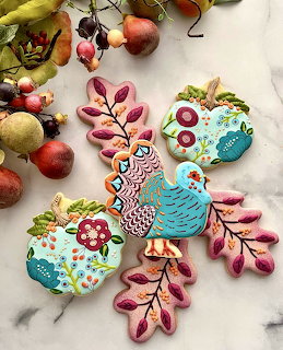 Decorated turkey-shaped cookies with colorful icing on marble surface surrounded by autumn leaves and apples