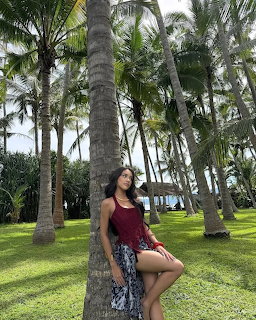 Woman posing on grass beneath tall palm trees in a tropical garden