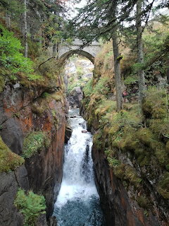 Stone arch bridge over a narrow gorge with waterfall flowing between rocky moss-covered cliffs