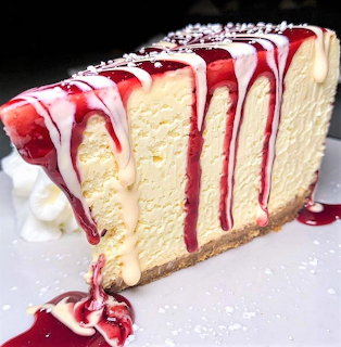 Slice of cheesecake with strawberry topping and red sauce drizzle on white plate