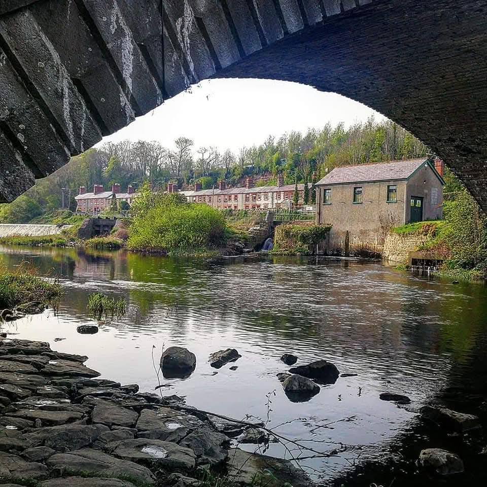 Stone arch bridge framing riverside buildings and trees in Lucan, Ireland