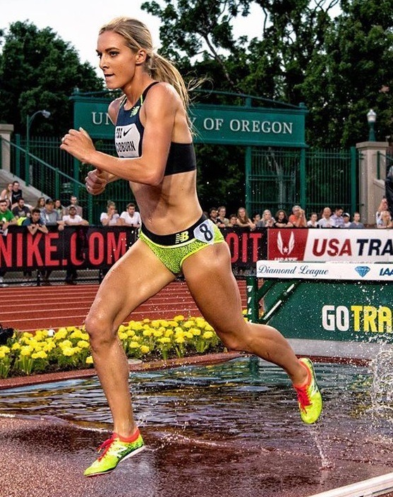 Female runner sprinting on a wet track at a stadium event wearing black top and yellow-green shorts