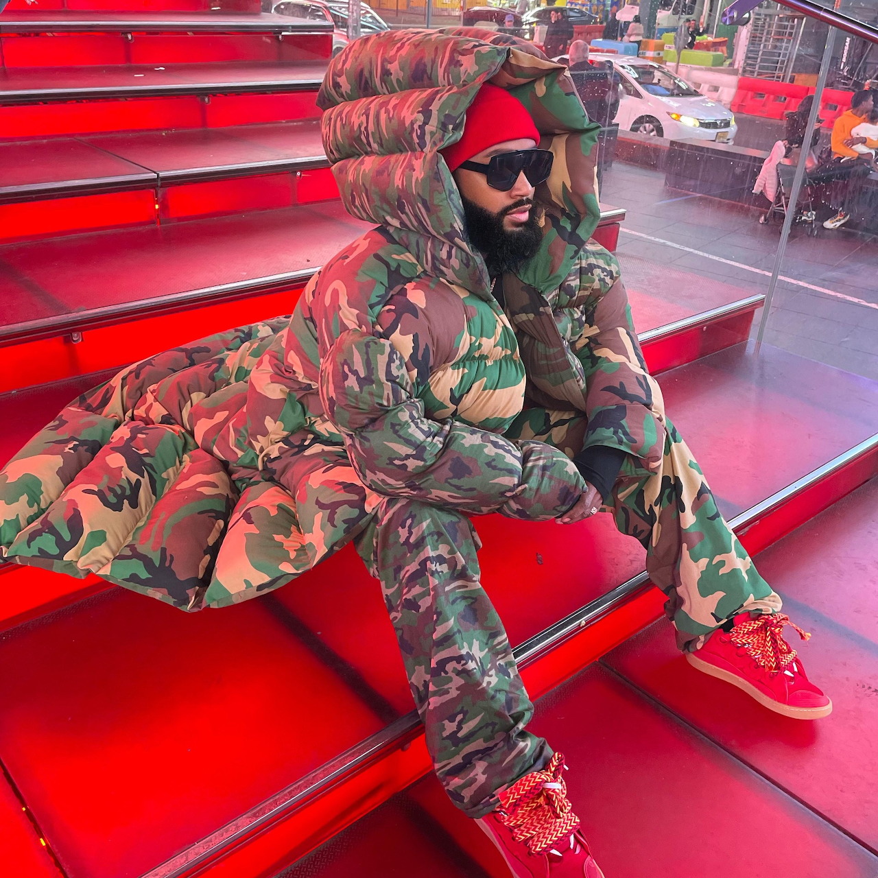 Man in camouflage winter outfit and sunglasses sitting on glowing red steps