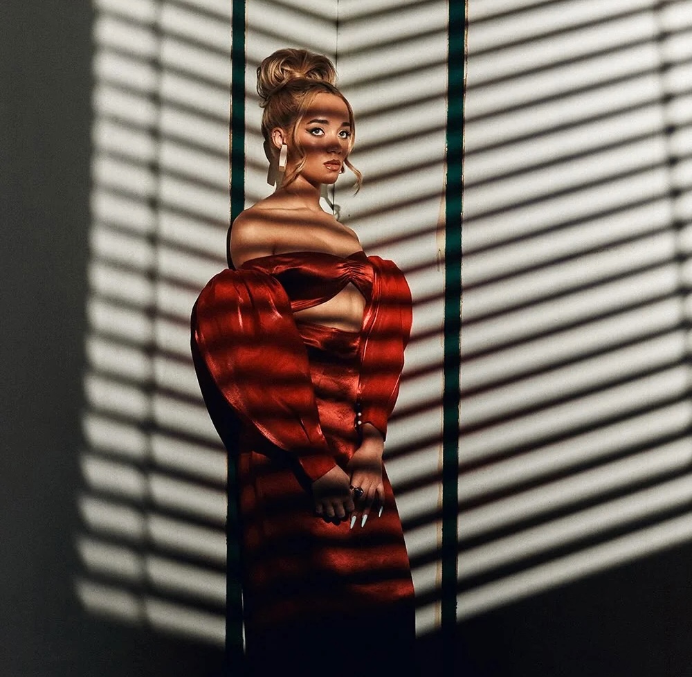 Woman in red dress posing with striped shadow patterns from venetian blinds