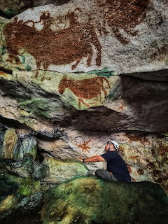 Ancient rock art with reddish-brown paintings on textured cave wall showing weathered stone and mineral deposits