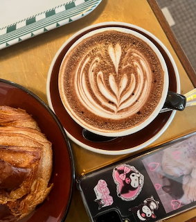 Coffee cup with leaf latte art on gold tray next to croissant and Kuromi phone case