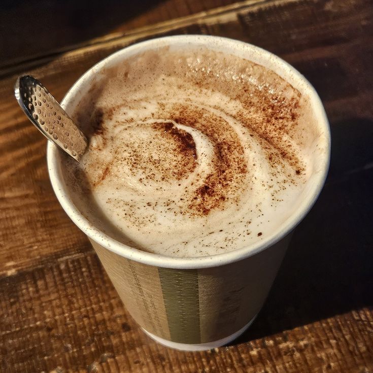 White cup of cappuccino with cinnamon swirl on foam, wooden spoon, dark wood table