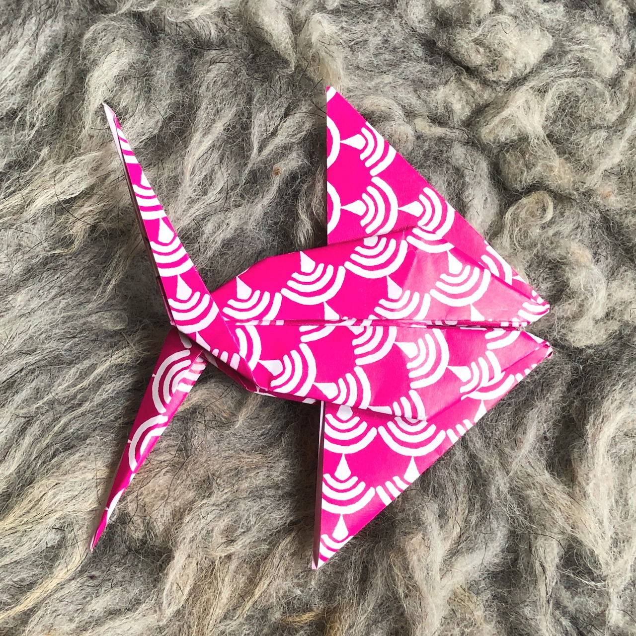 Pink patterned origami angelfish on a gray wool background