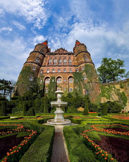 Historic ivy-covered castle with round towers above a formal garden with hedges and tulips