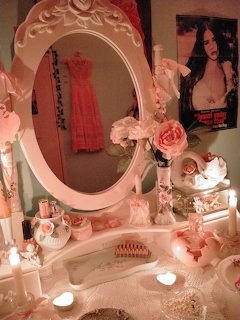 Pink vanity table with oval mirror, candles, roses, and beauty accessories