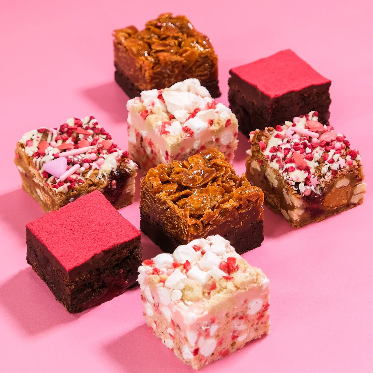Assortment of decorated brownie squares with toppings on pink background