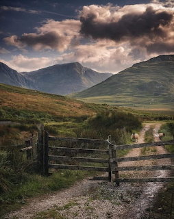 Dark storm clouds over green mountain valley with dirt path and wooden gate in Connemara countryside