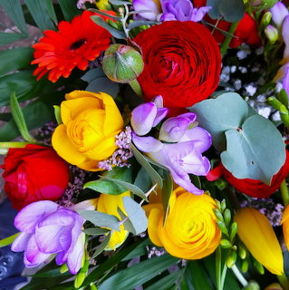 Close-up of a vibrant bouquet with red, yellow, and purple flowers including roses, ranunculus, and freesias